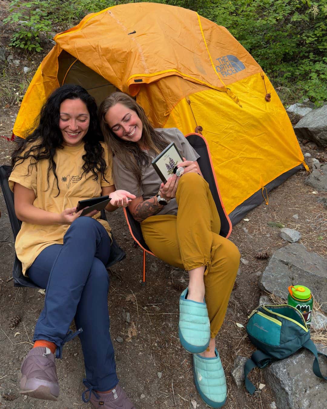 Two friends wearing their favorite Coalatree Trailhead pants while reading at their campsite.