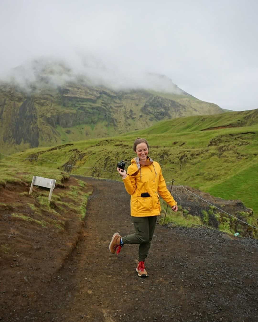 A woman standing on a hiking trail in Iceland with a bright yellow jacket and her favorite green joggers that are perfect for all types of travel.