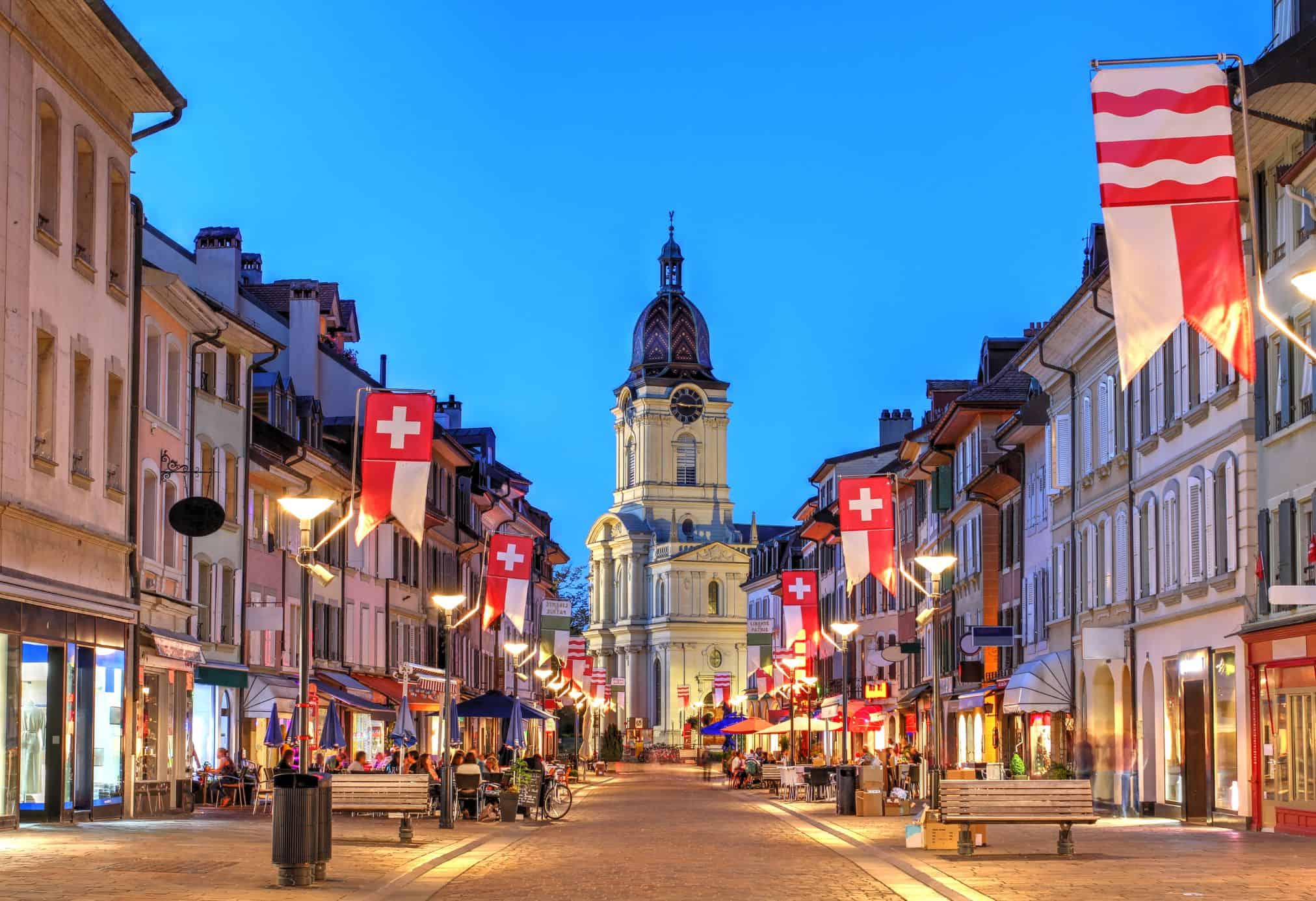 Lausanne, Switzerland at night with Swiss flags and sidewalk lights illuminating the city on a beautiful evening.