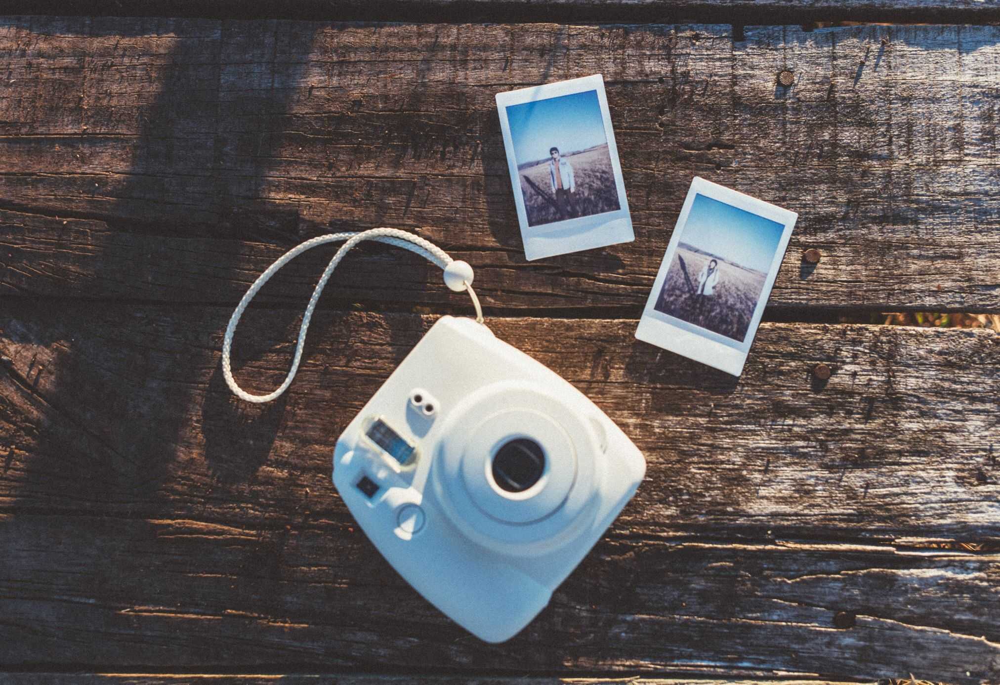 A polaroid camera sitting on a picnic table with a couple of photos printed out.