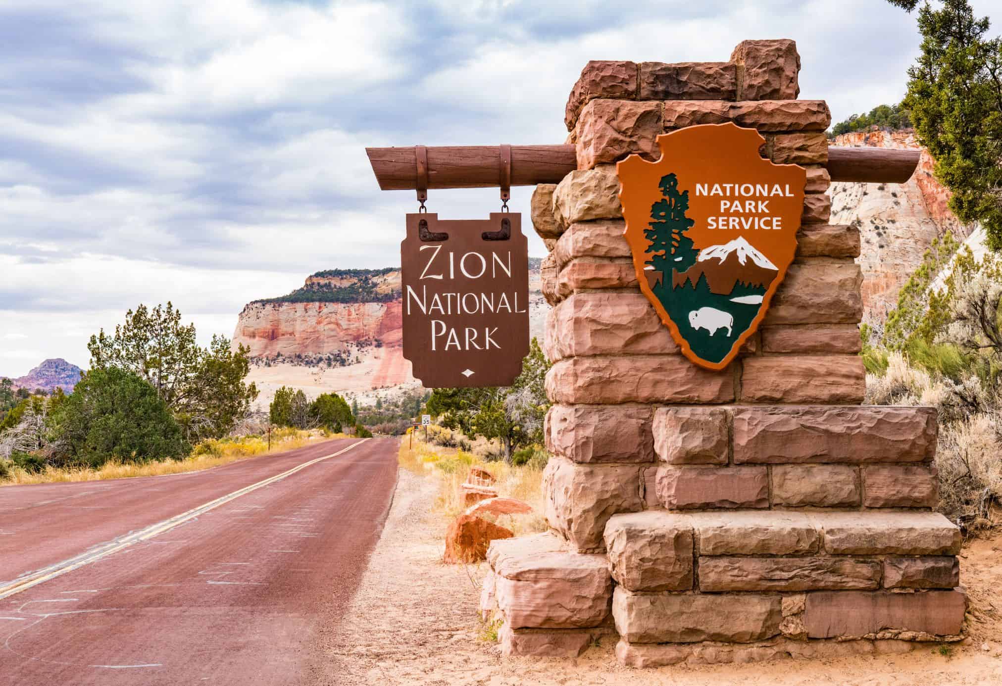A sign to Zion National Park on a beautiful day. The National Park Pass is a great gift for road trippers because of how expensive entry fees can be when they add up.