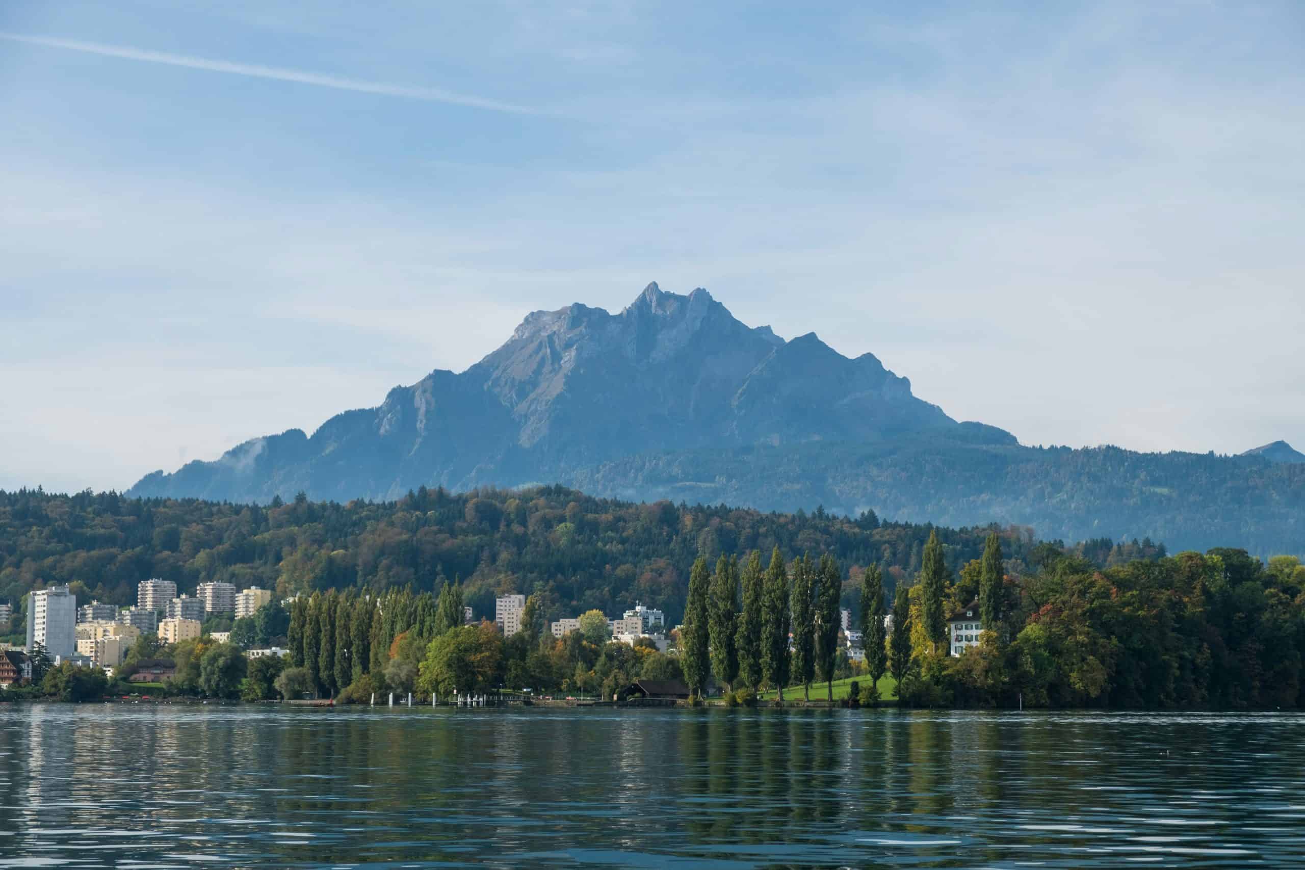 A view of the mountains from the city with Lake Lucerne in the photo and the buildings reflecting off the water.