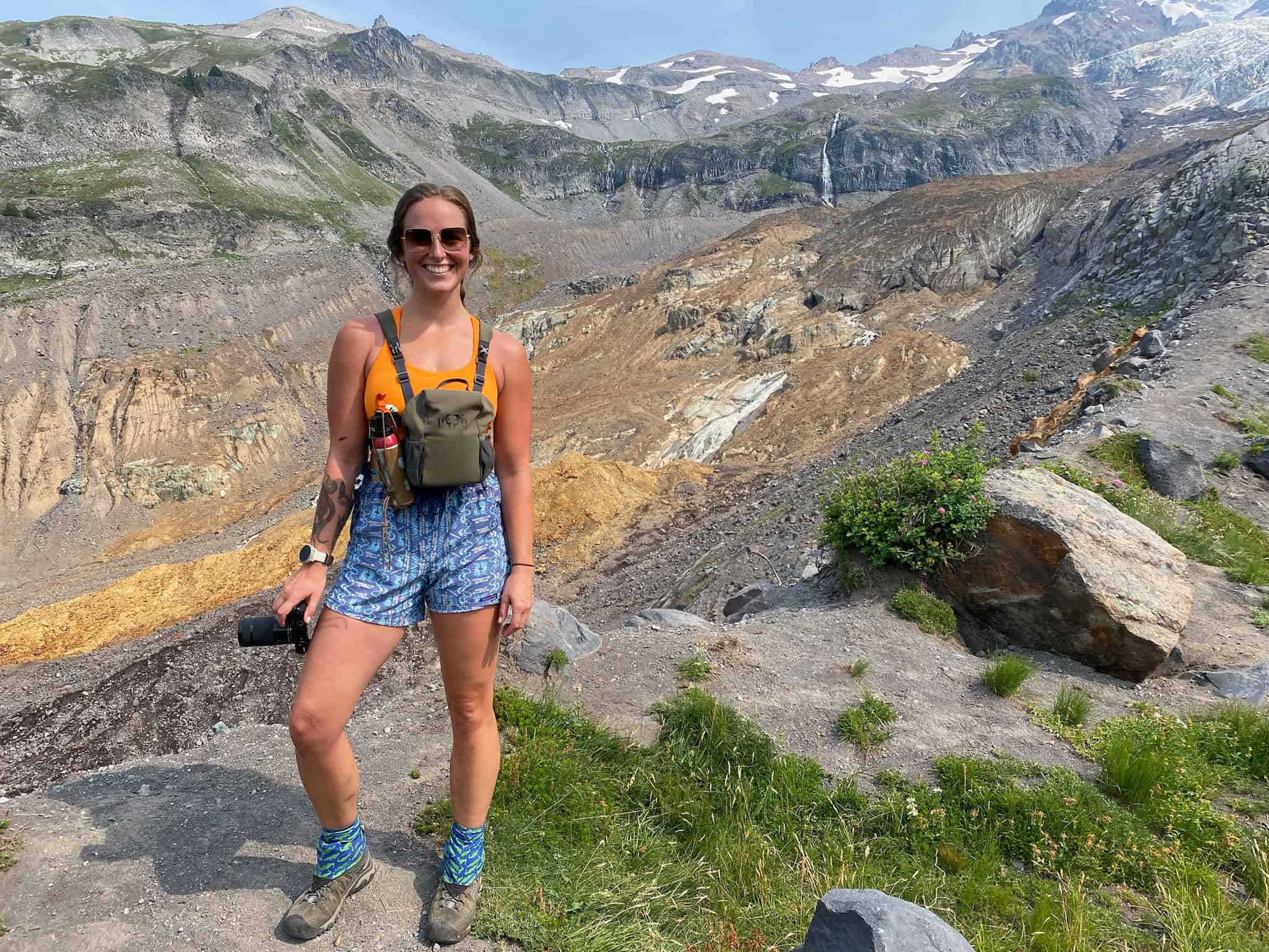 A woman standing on a hiking trail on Mount Rainier on a hot summer day. This woman is wearing KEEN hiking boots, some of the best women's hiking boots out there!