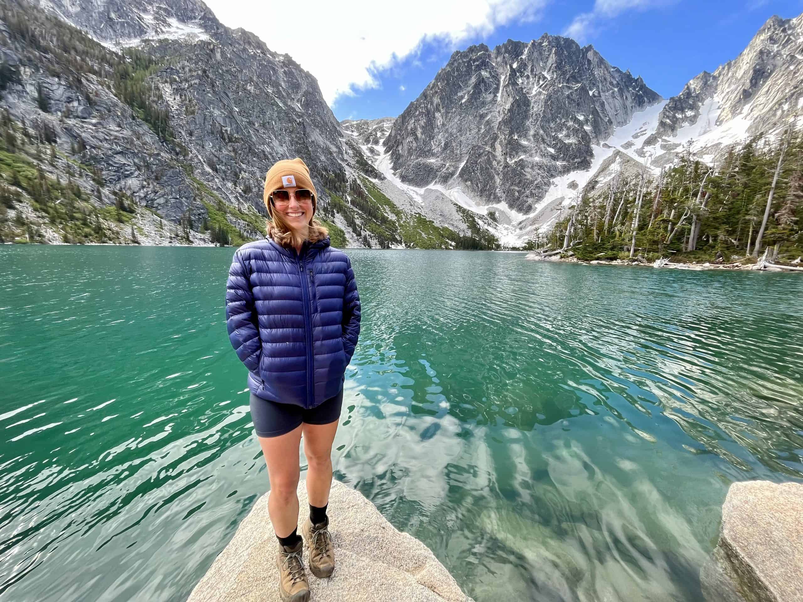 A woman standing in front of a lake in Washington State wearing KEEN boots. These are some of the best women's hiking boots in 2025 for multiple reasons.