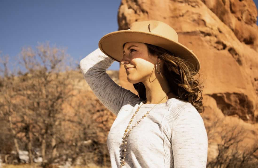 A woman standing in a light sweater with a wool hat in the fall on a crisp bluebird day.