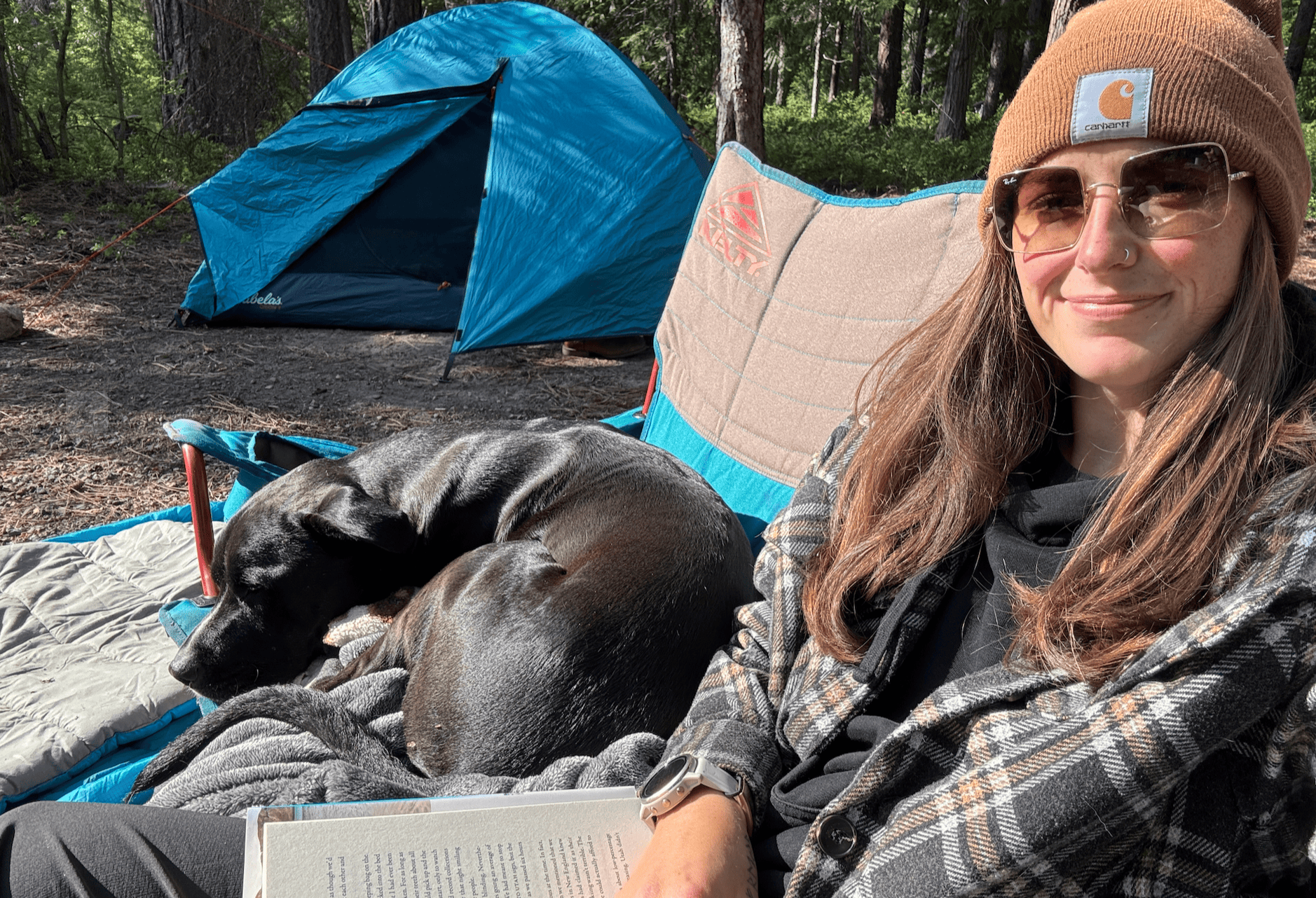 A woman bundled up in her warm clothing on a fall morning while camping with her dog.