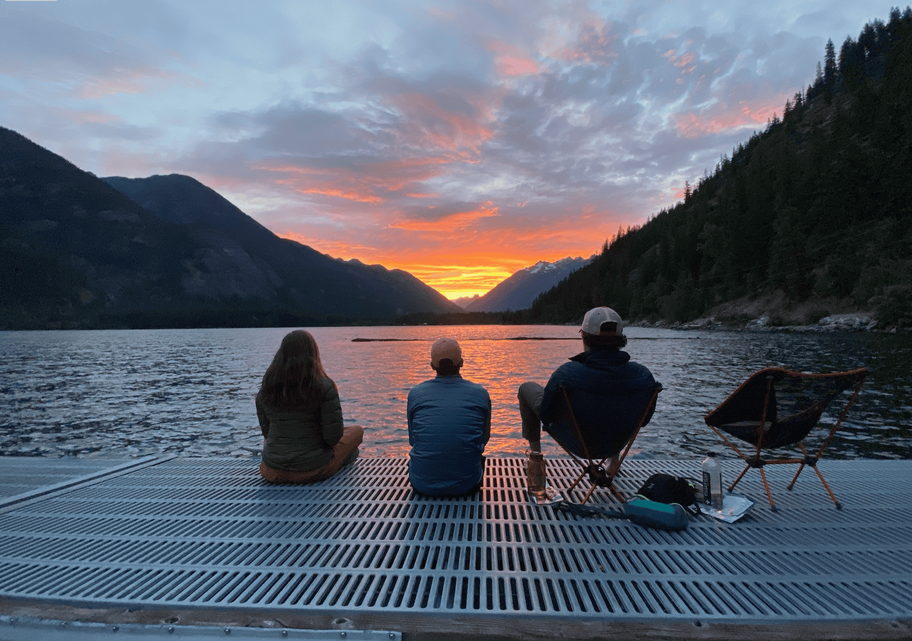 Three friends sitting on a dock at sunset admiring the sun that is slowly going down behind the mountains.