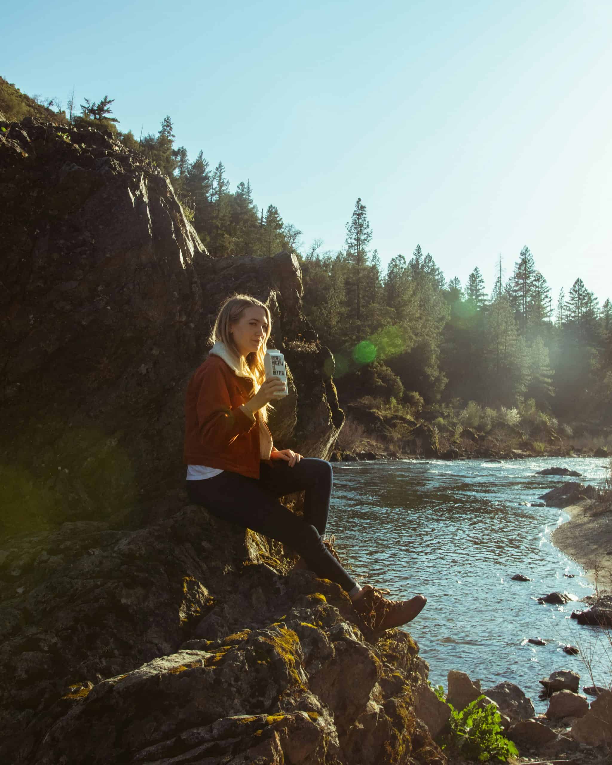 A woman sitting on rocks right next to the ocean on a beautiful day. She is showing the perfect outfit for what to wear in Seattle in the fall. A warm jacket, leggings, and boots is the perfect outfit while visiting Seattle in the fall.