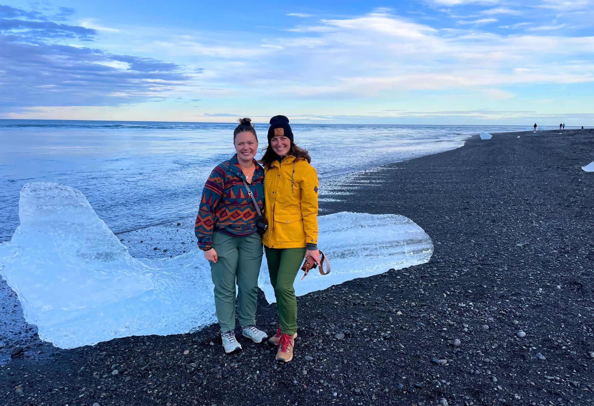 Two girl friends who are on Diamond Beach in Iceland during a late august tirp. They are dressed in clothes that are warmer, and this is a must for a Iceland packing list.