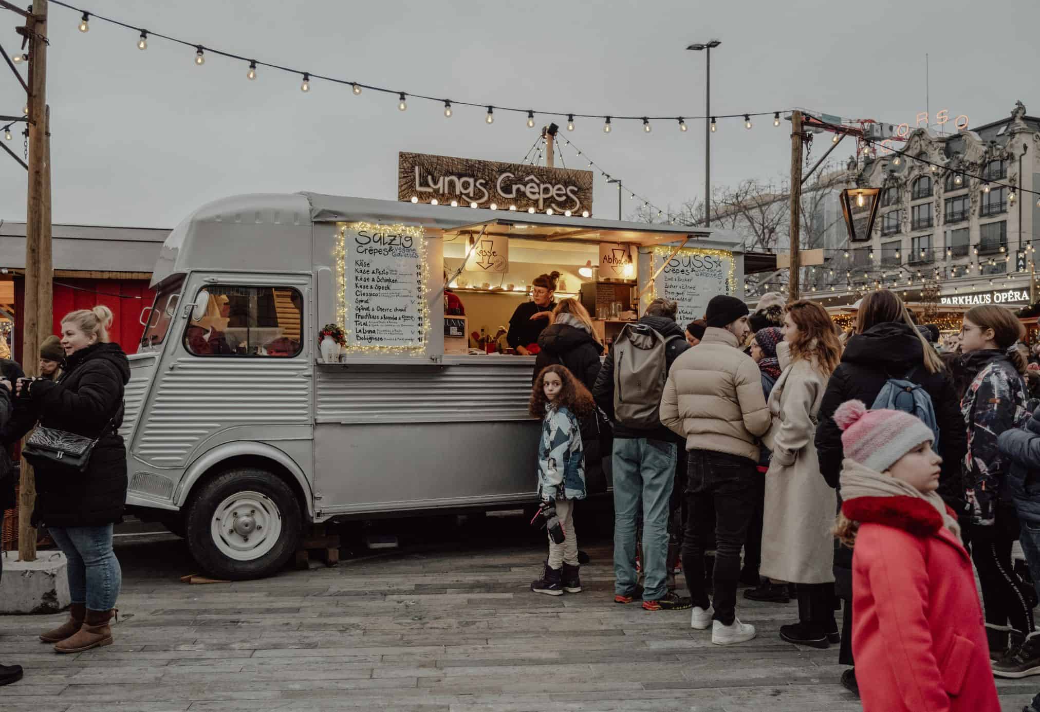 A crepe truck in one of the Christmas markets in Zurich. There are a line of people all bundled up to stay warm in the chilly air.