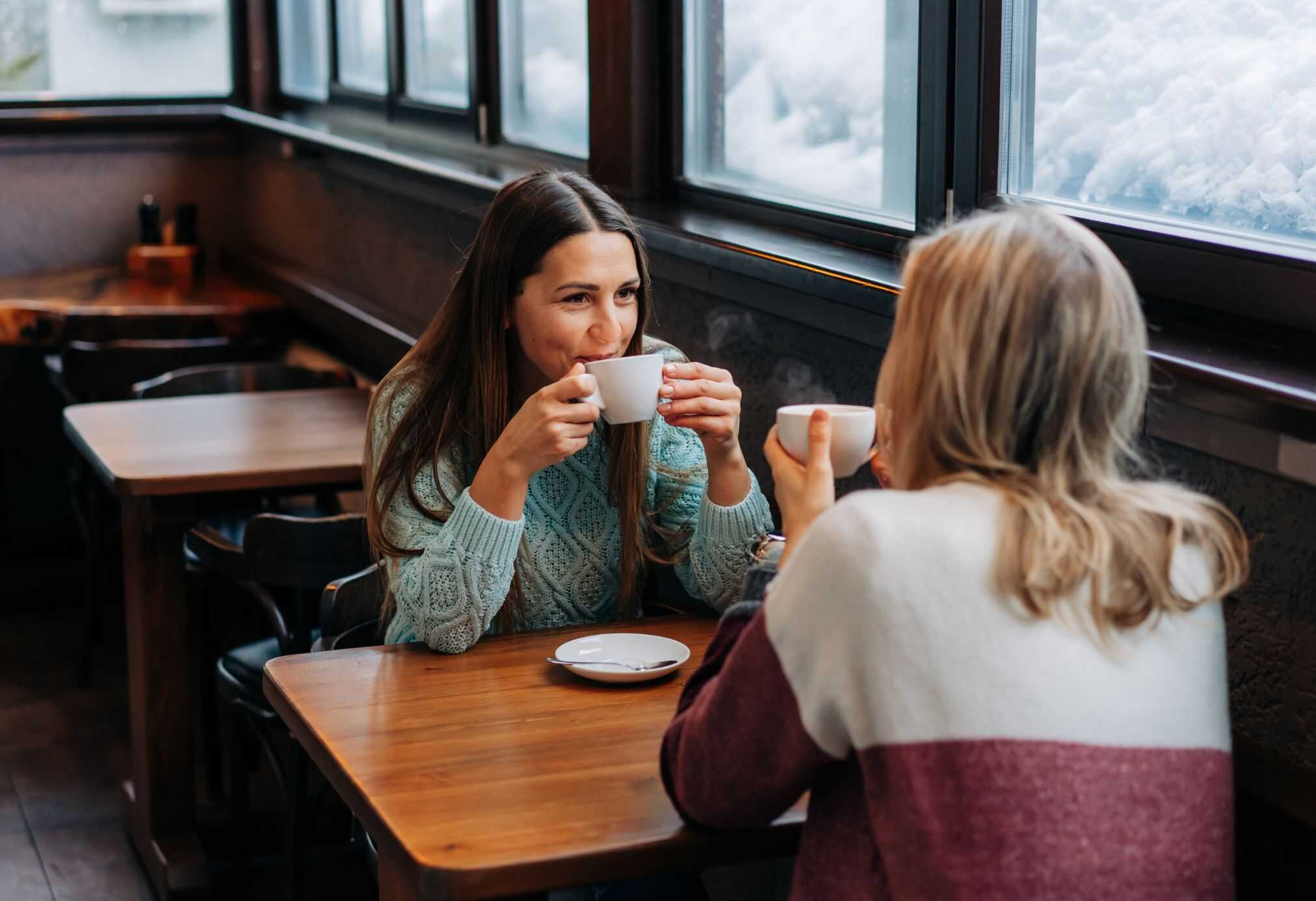 Two women drinking lattes at one of the cozy cafes in Switzerland on a snowy day.
