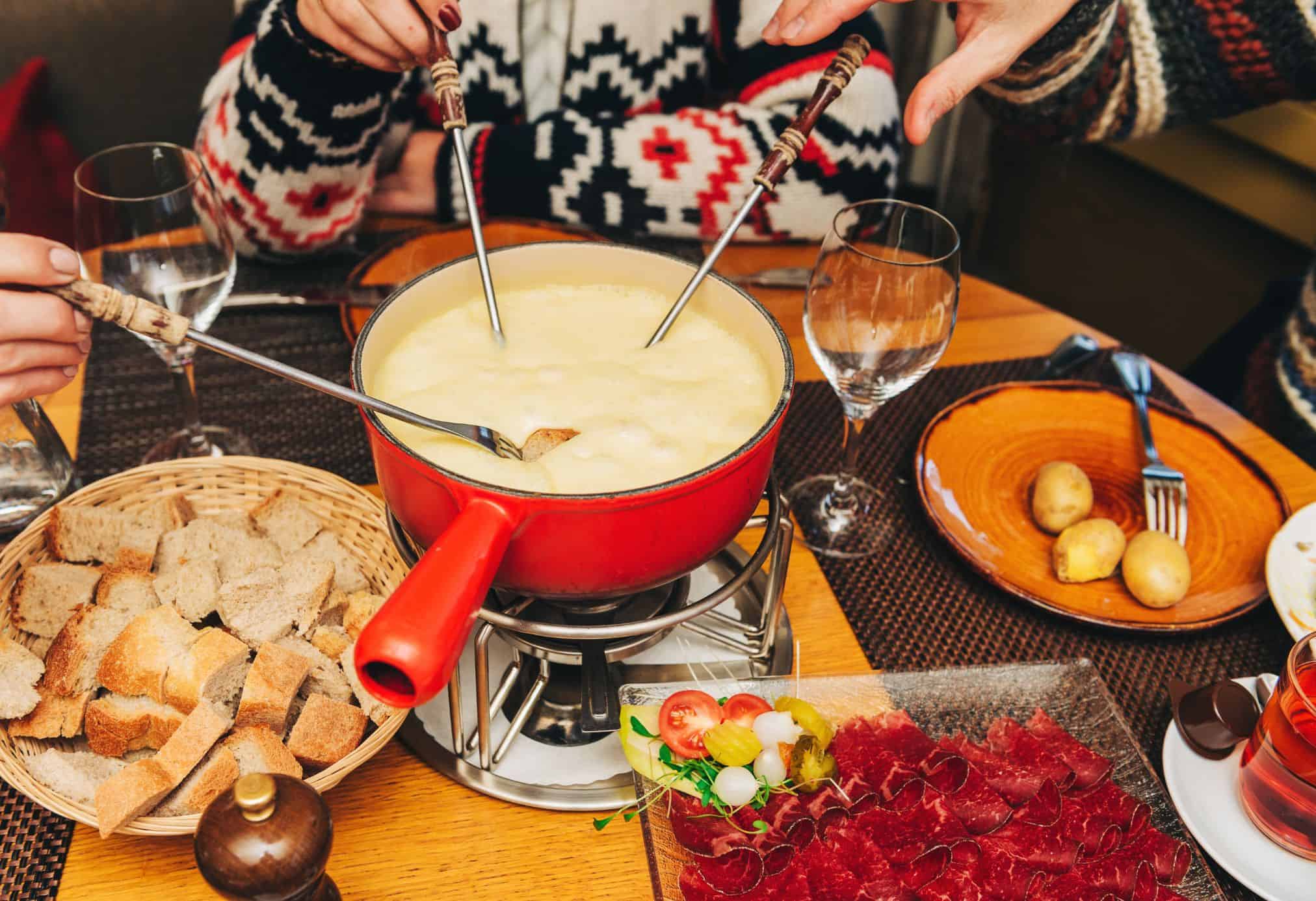 Friends gathering together for a delicious meal of fondue at a cozy restaurant in Switzerland.