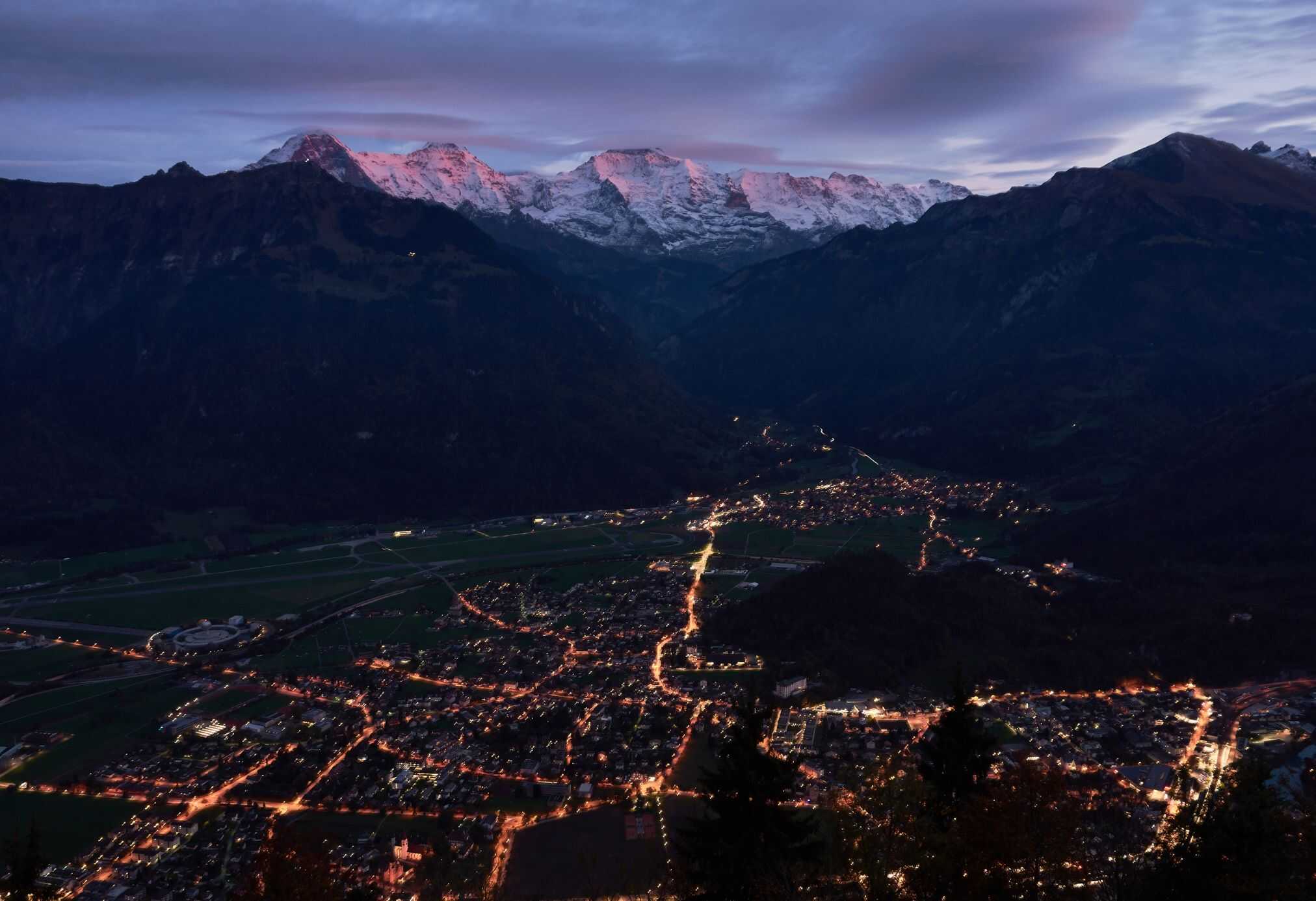 Interlaken in the winter shows off the city lights and pink brushed mountains at the lookout on Harder Kulm.