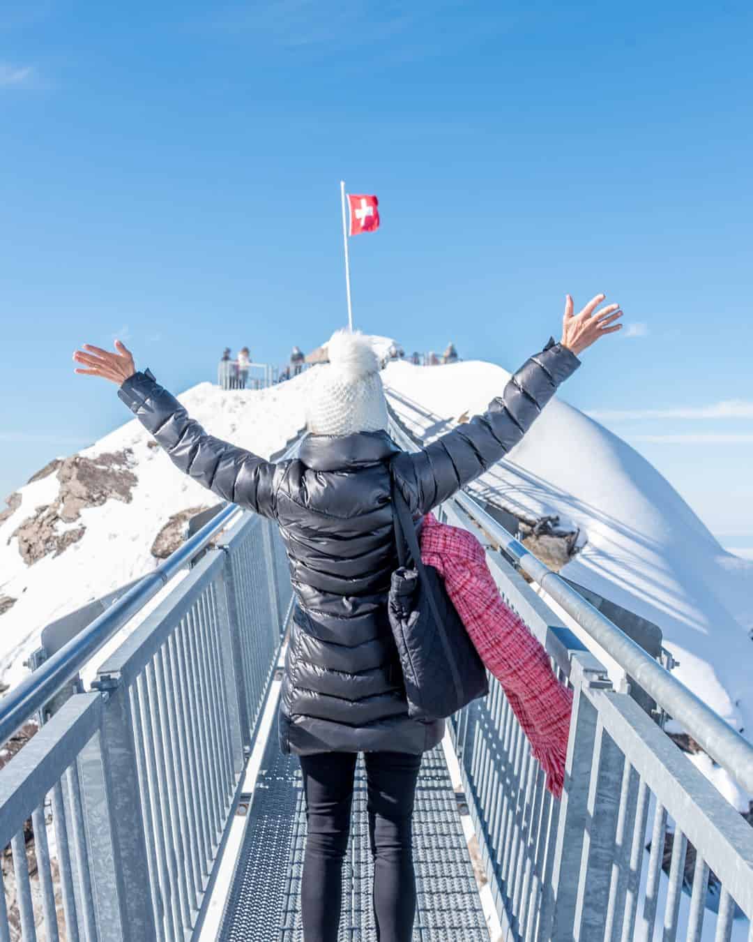 A woman in a puffy jacket standing on one of Switzerland's most iconic  walk in the mountains.