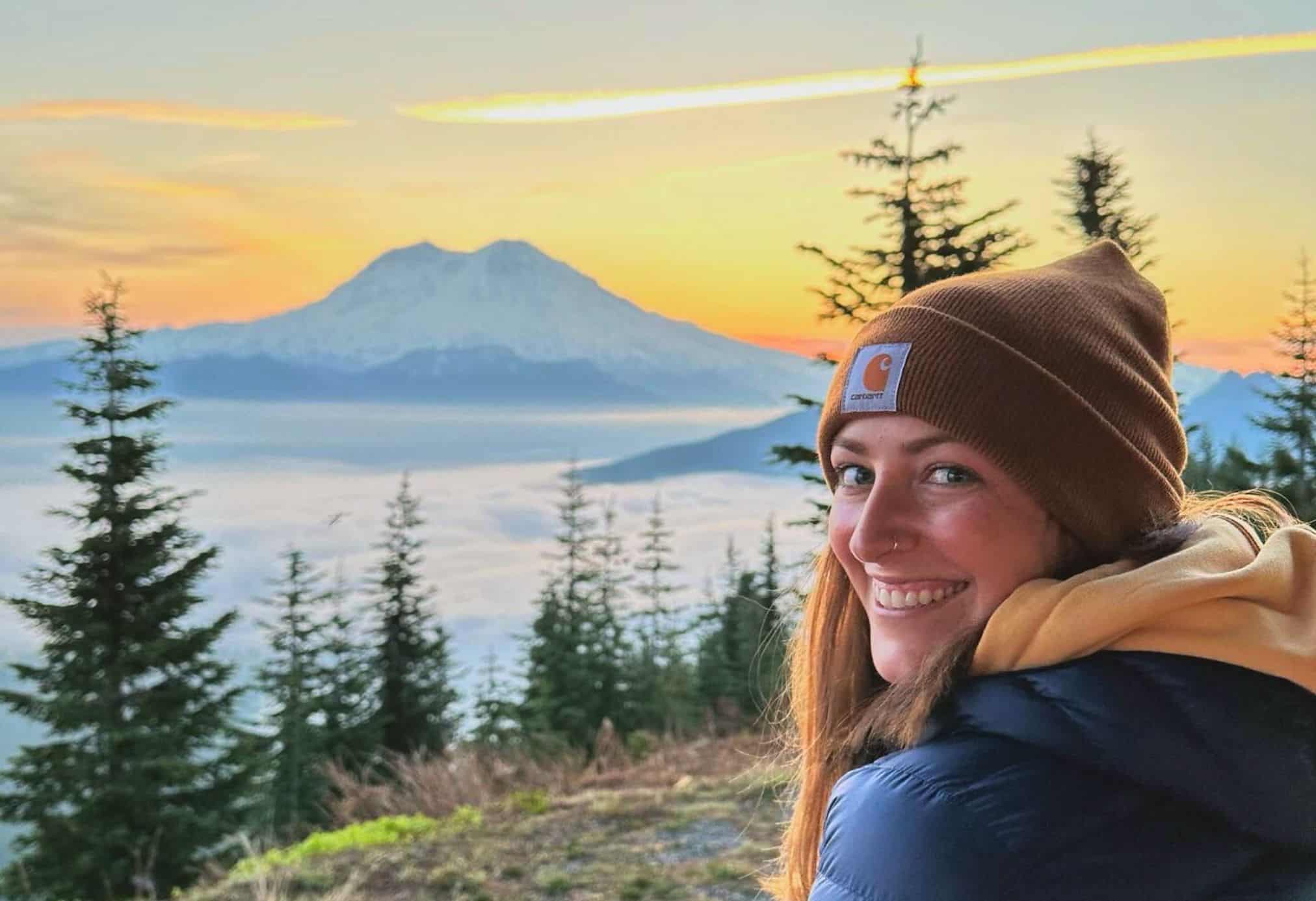 A woman standing at sunrise with Mt. Rainier in the background wearing a Carhartt beanie to stay warm on a chilly morning.